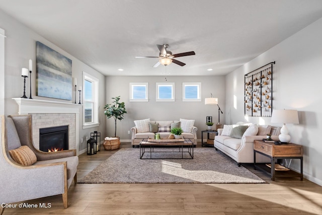 living room with wood finished floors, a brick fireplace, a ceiling fan, and plenty of natural light