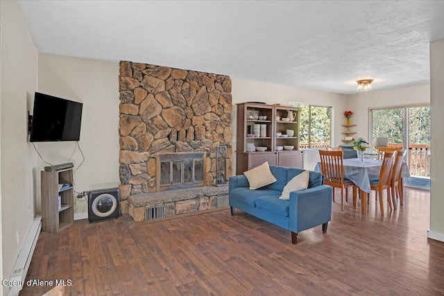 living room with a fireplace, visible vents, a textured ceiling, wood finished floors, and a baseboard radiator