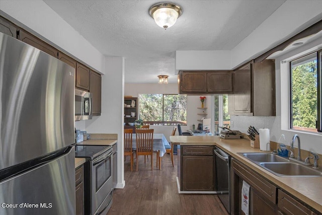 kitchen featuring a textured ceiling, a sink, appliances with stainless steel finishes, dark wood-style floors, and a peninsula