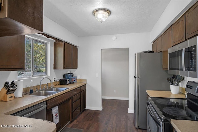 kitchen with stainless steel appliances, light countertops, a sink, baseboards, and dark wood-type flooring