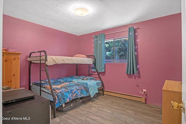 bedroom featuring a textured ceiling, wood finished floors, a textured wall, and baseboard heating