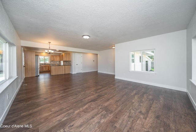 unfurnished living room featuring dark wood finished floors, an inviting chandelier, a textured ceiling, and baseboards