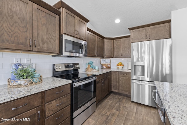 kitchen featuring dark brown cabinets, appliances with stainless steel finishes, light stone counters, lofted ceiling, and dark wood-style floors