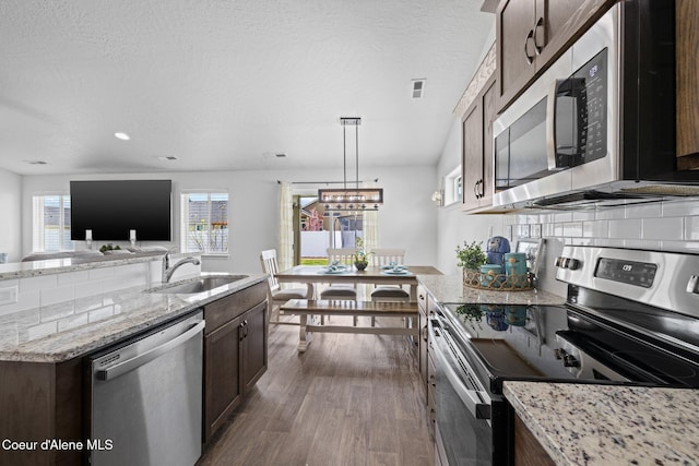 kitchen featuring light stone countertops, dark brown cabinetry, appliances with stainless steel finishes, a sink, and dark wood-type flooring