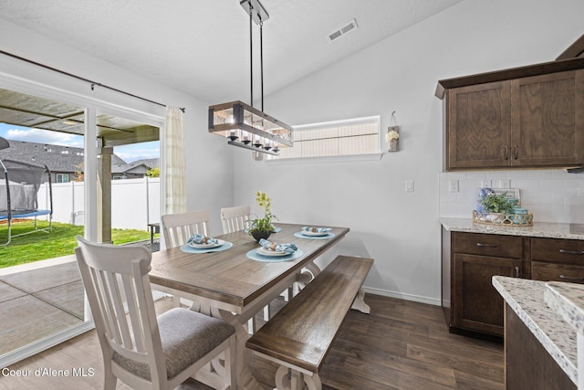 dining room featuring dark wood-type flooring, lofted ceiling, visible vents, and an inviting chandelier