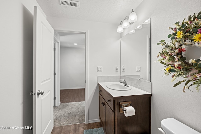 bathroom with vanity, toilet, decorative backsplash, wood finished floors, and visible vents