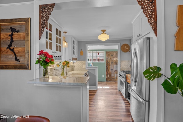 kitchen featuring dark wood-style flooring, appliances with stainless steel finishes, tasteful backsplash, light stone counters, and glass insert cabinets