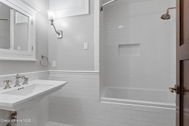 bathroom with a sink, tile walls, tiled shower / bath, and wainscoting
