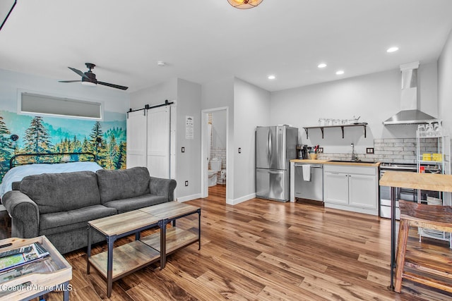 living room featuring baseboards, recessed lighting, a barn door, a ceiling fan, and light wood-style flooring