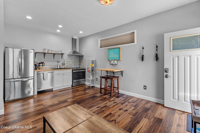 kitchen with wall chimney range hood, recessed lighting, dark wood-type flooring, a sink, and stainless steel appliances