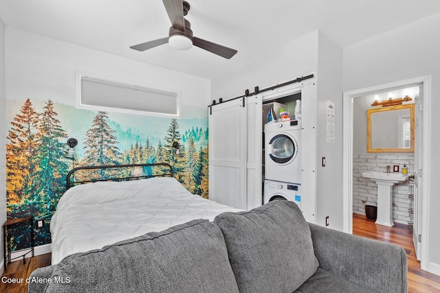 bedroom featuring a sink, wood finished floors, stacked washing maching and dryer, a barn door, and a ceiling fan