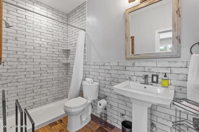 bathroom with wood finished floors, a stall shower, toilet, and a wainscoted wall
