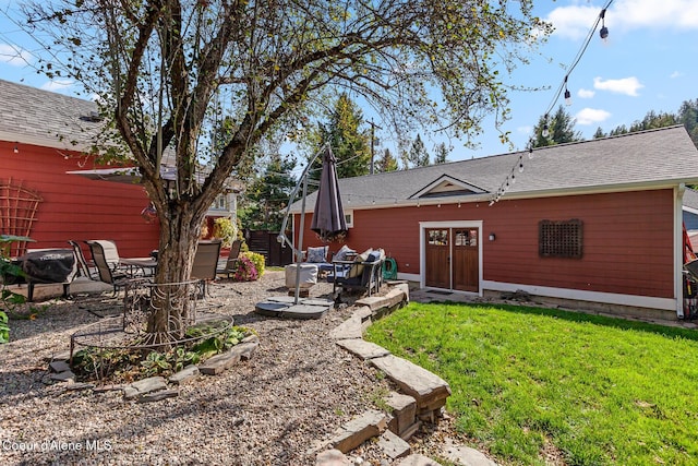 rear view of property featuring a lawn, a patio, and a shingled roof