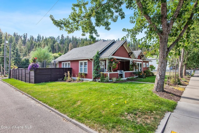 view of front of property with fence, a shingled roof, and a front lawn
