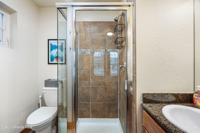 full bath featuring toilet, a textured wall, vanity, and a stall shower