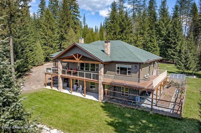rear view of house featuring a deck, a chimney, a shingled roof, a patio area, and a lawn