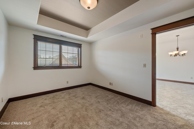 carpeted empty room featuring baseboards, a tray ceiling, a chandelier, and visible vents