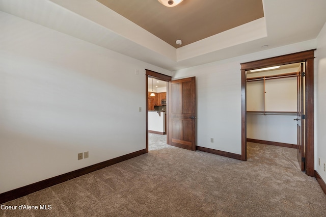 unfurnished bedroom with baseboards, carpet, a tray ceiling, and a spacious closet