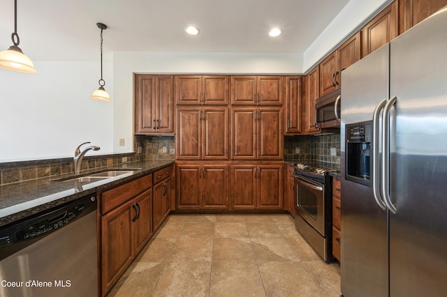 kitchen with appliances with stainless steel finishes, a sink, dark stone counters, decorative light fixtures, and backsplash