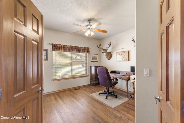 office featuring baseboards, a ceiling fan, light wood-style flooring, and a textured ceiling