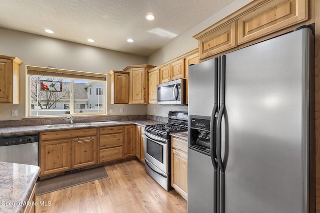 kitchen featuring recessed lighting, a textured ceiling, a sink, light wood finished floors, and stainless steel appliances