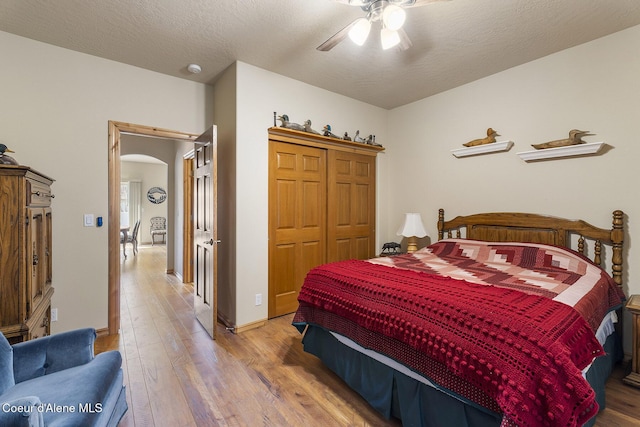 bedroom with arched walkways, a ceiling fan, baseboards, wood finished floors, and a closet