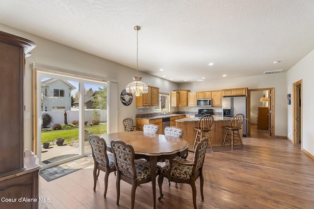 dining room featuring wood-type flooring, recessed lighting, a textured ceiling, and visible vents