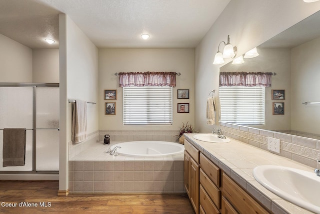 full bath with a sink, double vanity, wood finished floors, a bath, and a stall shower