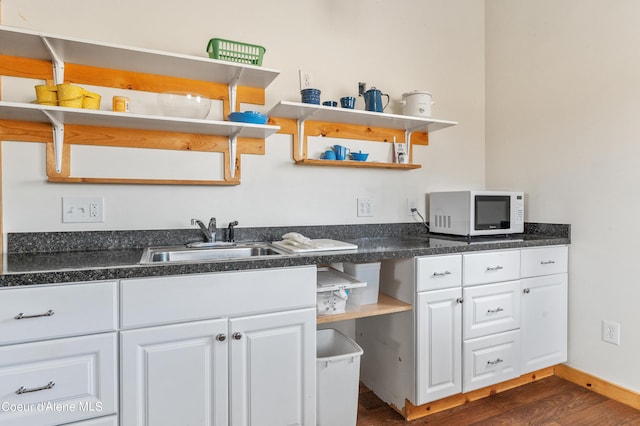 kitchen with dark wood finished floors, open shelves, a sink, white microwave, and white cabinetry