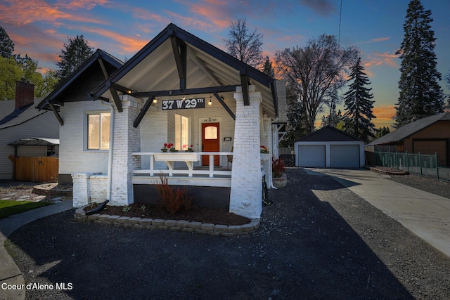 view of front of home with an outbuilding, a porch, fence, brick siding, and a garage