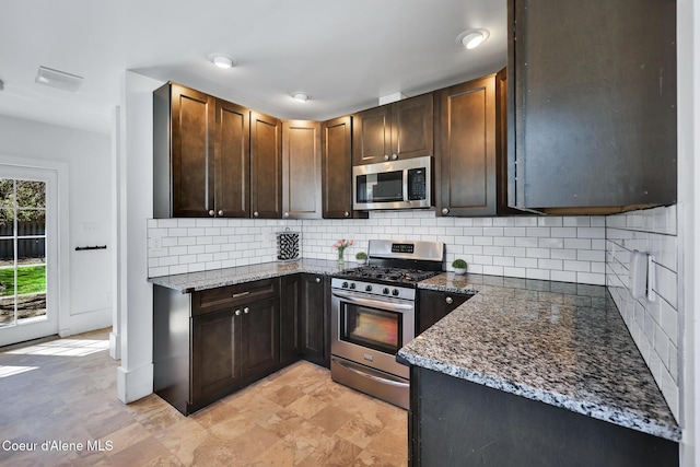 kitchen featuring stainless steel appliances, dark brown cabinetry, dark stone counters, and tasteful backsplash