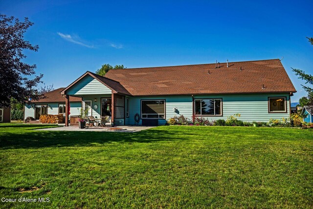 back of property with a yard, a patio area, and a shingled roof
