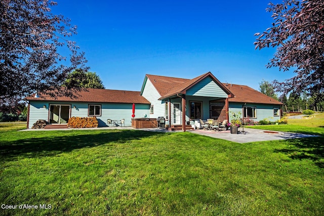 rear view of property with a yard, a hot tub, and a patio