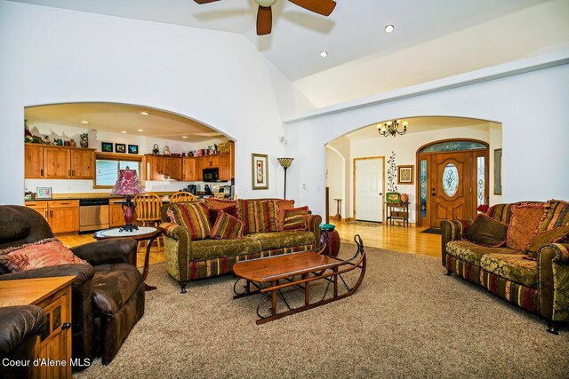 living room with light wood finished floors, arched walkways, recessed lighting, ceiling fan with notable chandelier, and high vaulted ceiling
