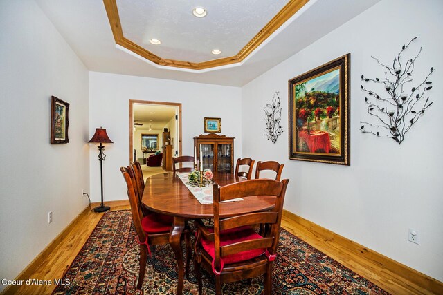 dining space with a tray ceiling, baseboards, recessed lighting, light wood-style floors, and crown molding