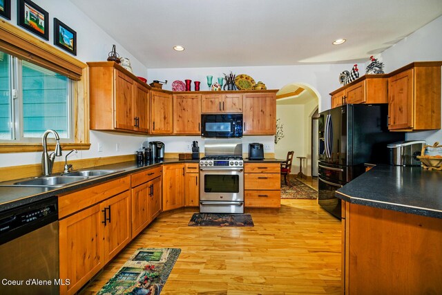 kitchen with dark countertops, a sink, arched walkways, light wood-style floors, and black appliances
