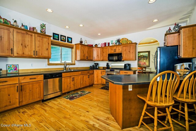 kitchen featuring dark countertops, a sink, brown cabinets, stainless steel appliances, and light wood finished floors