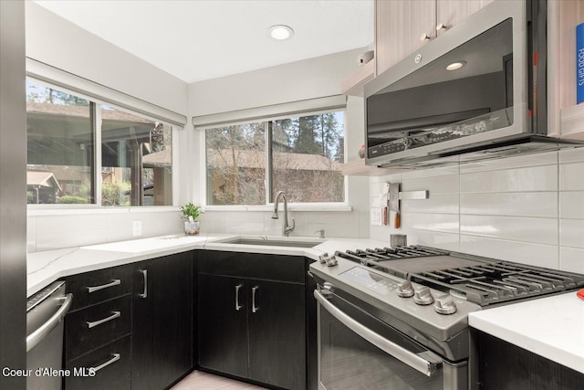 kitchen with backsplash, light stone countertops, a sink, dark cabinetry, and stainless steel appliances