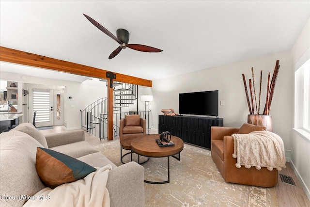 living area with a ceiling fan, visible vents, stairway, baseboards, and beamed ceiling