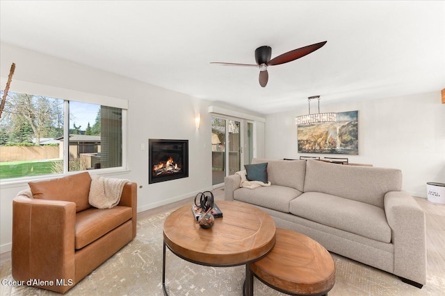 living area with a glass covered fireplace, baseboards, and a ceiling fan