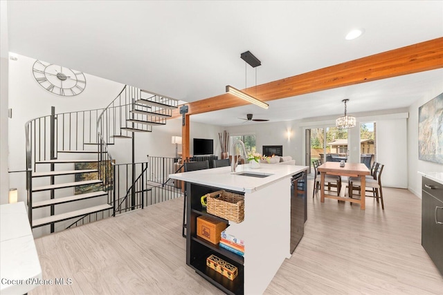 kitchen featuring a sink, light countertops, light wood-style flooring, ceiling fan with notable chandelier, and open floor plan