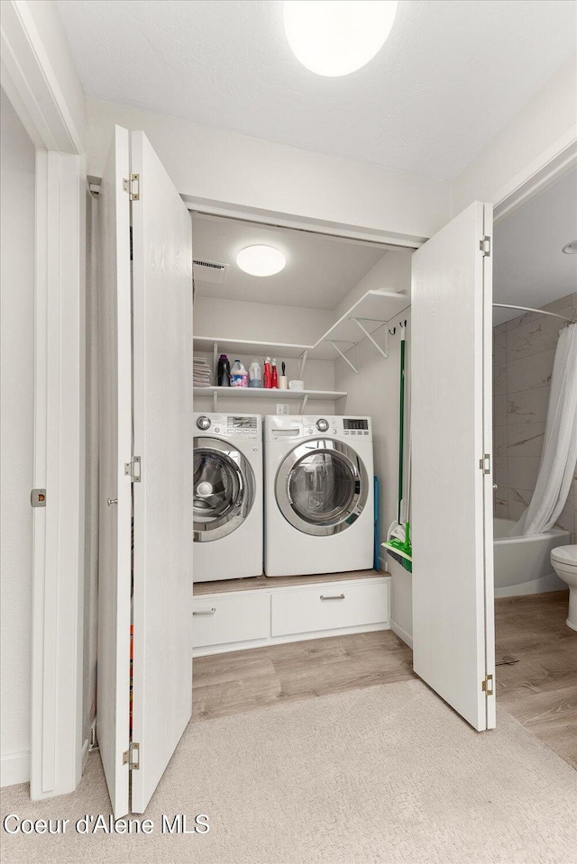 clothes washing area featuring separate washer and dryer, laundry area, wood finished floors, and visible vents