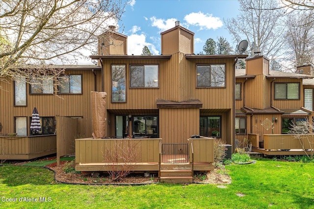 back of house featuring a lawn, a chimney, and a deck