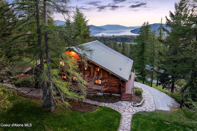 view of side of property featuring metal roof, a lawn, a wooded view, log exterior, and a mountain view
