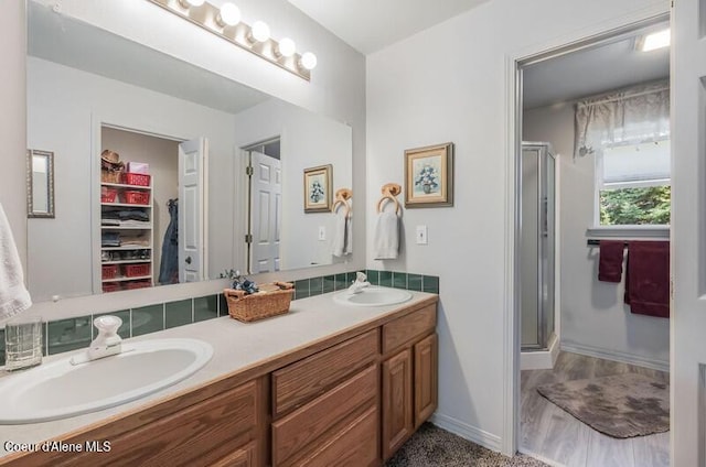 bathroom featuring a sink, double vanity, a stall shower, and baseboards