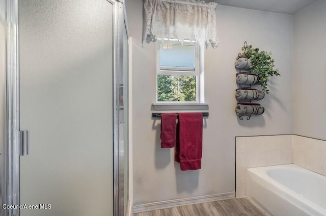 bathroom featuring a stall shower, baseboards, a garden tub, and wood finished floors