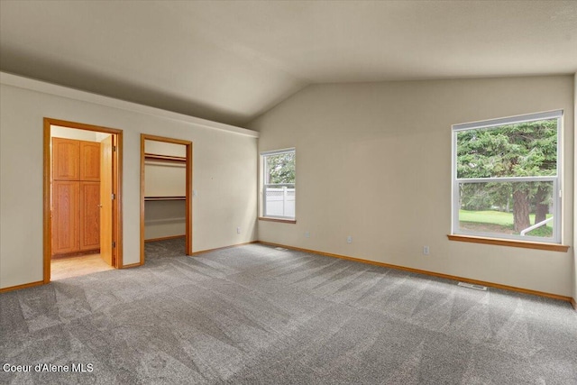 unfurnished bedroom featuring vaulted ceiling, carpet floors, a spacious closet, and baseboards