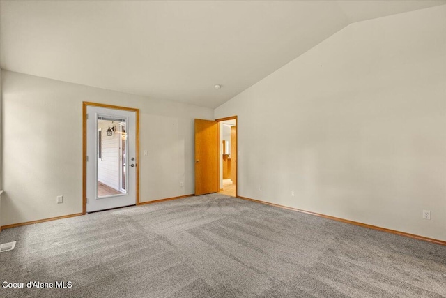 carpeted spare room featuring lofted ceiling and baseboards