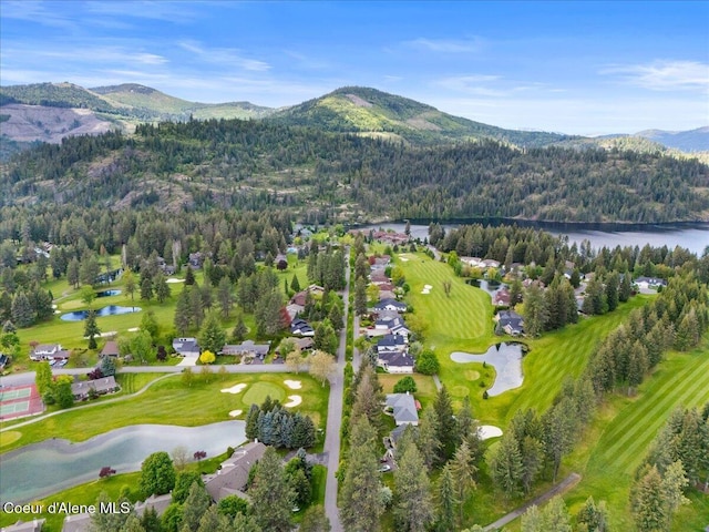 view of property location featuring a forest, a water and mountain view, and a local golf course