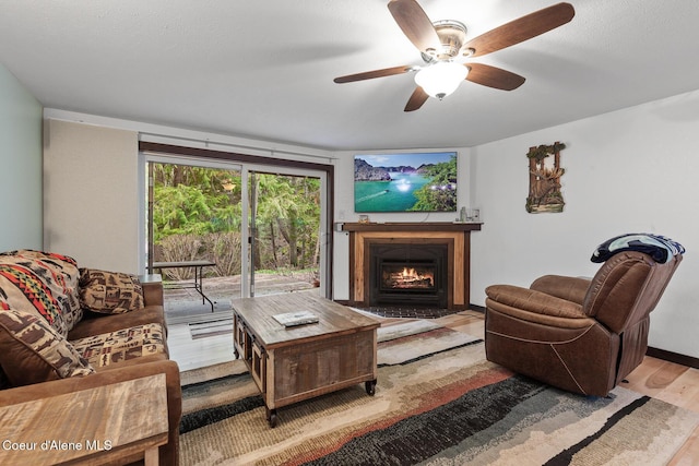 living area featuring a ceiling fan, a fireplace with flush hearth, and wood finished floors